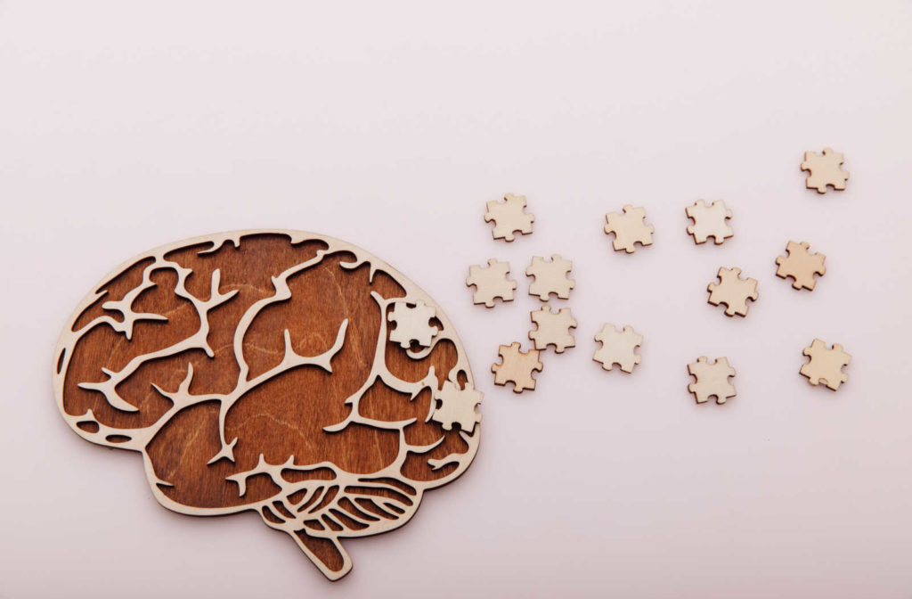 Wood cut out of a brain, with puzzle pieces laid around it.