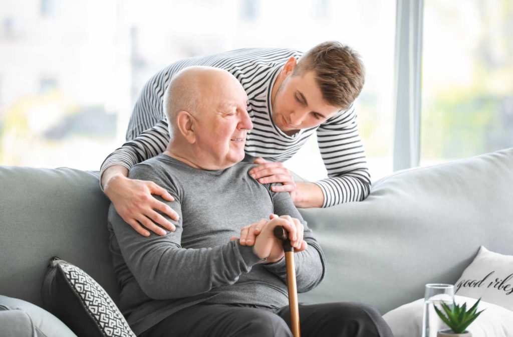 A young man checks in on his father who is sitting on the couch.