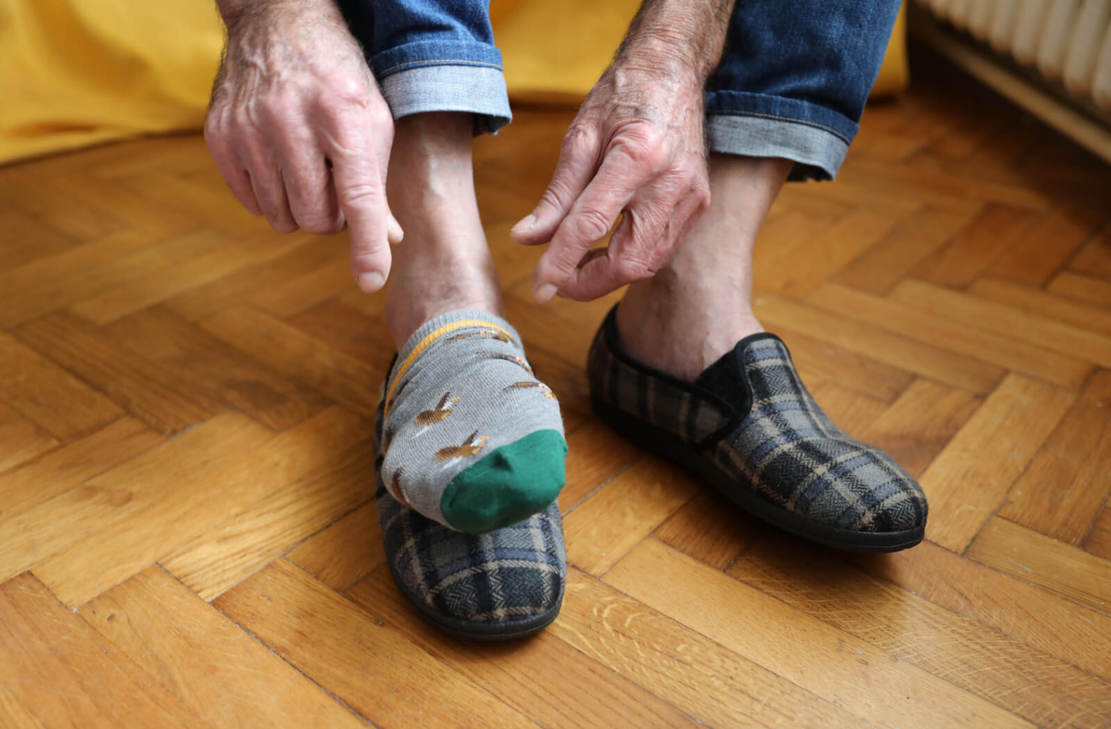 A senior man is putting socks on his right foot and putting them on his shoes.
