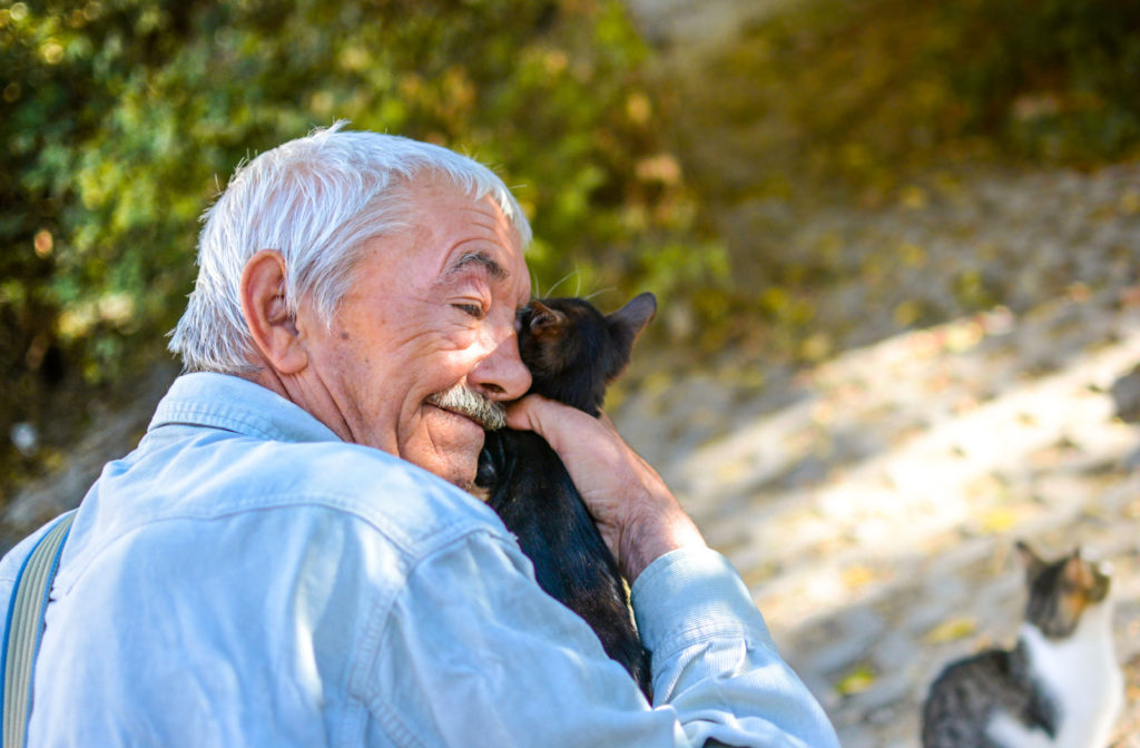 A senior man smiling and holding a kitten in his right hand in an animal shelter