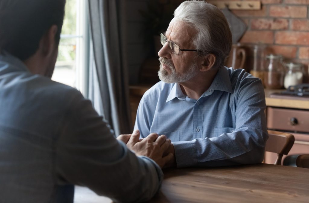 A person holding hands with his older parent at a table during a thoughtful discussion.