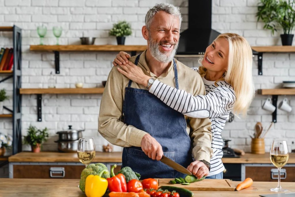 An older couple hugging in the kitchen while cutting vegetables for a brain-friendly meal.