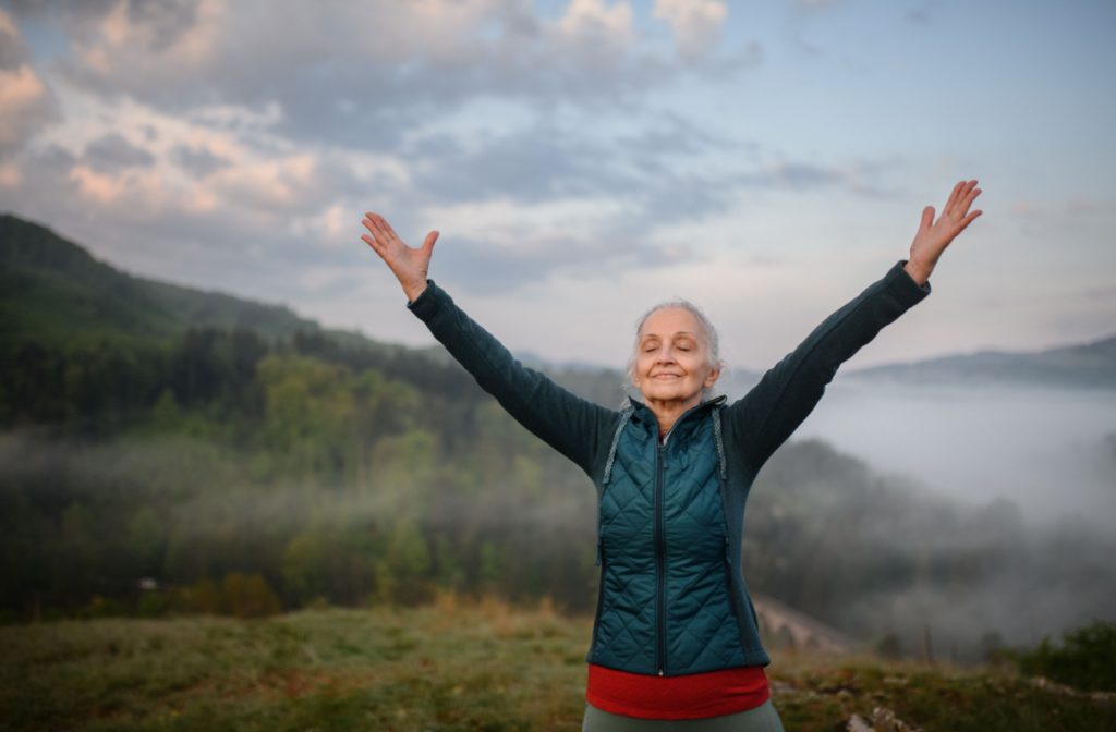 Senior enjoying the outdoors with arms raised practicing breathing exercises to enhance lung function and overall quality of life.