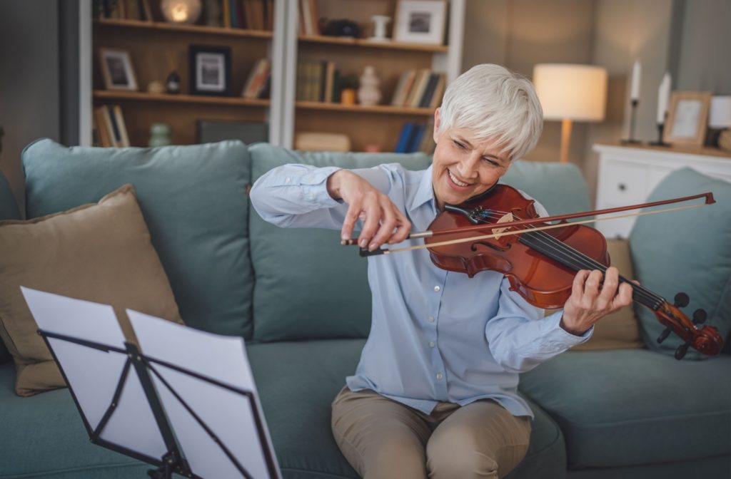 A senior practices the violin on their livingroom couch as part of their gentle morning routine.