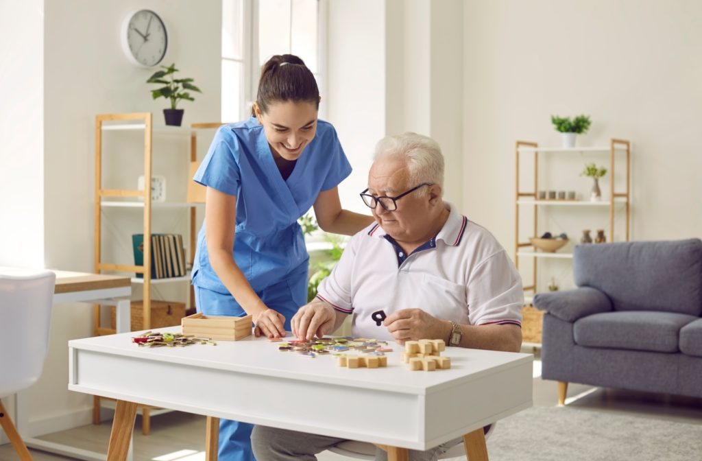 A senior doing a jigsaw puzzle accompanied by a nurse in their care facility.