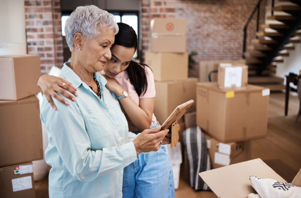 An older adult reminiscing over a photo with their grandchild while surrounded by moving boxes.