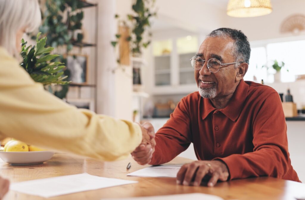 A senior shakes the hand of a senior living community representative while taking a tour of their living spaces