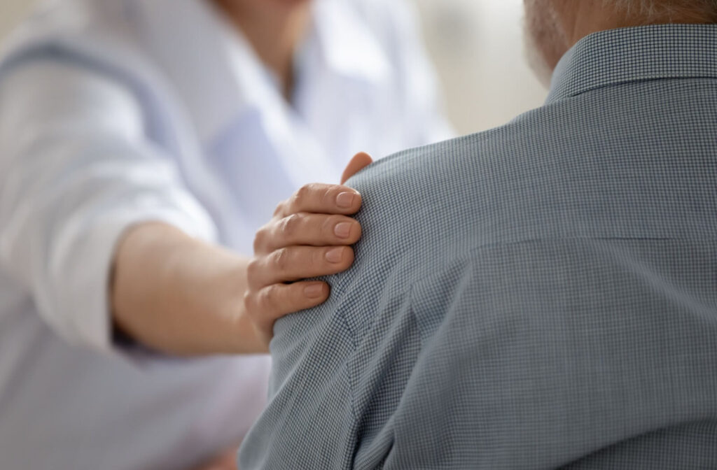 A caregiver places a hand on a senior’s shoulder to provide emotional support during their transition to memory care