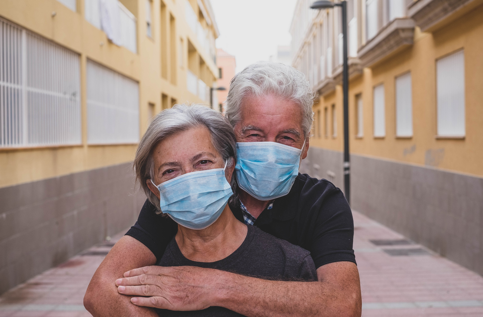 Senior couple hugging one another with their masks on their face.