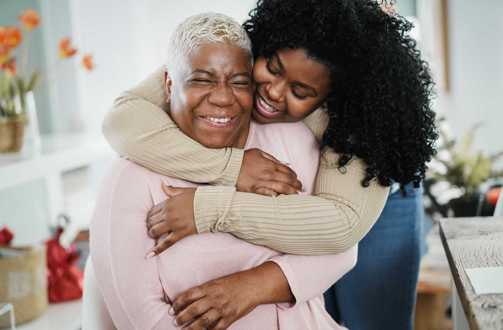 Smiling daughter hugging her happy elderly mother from behind.