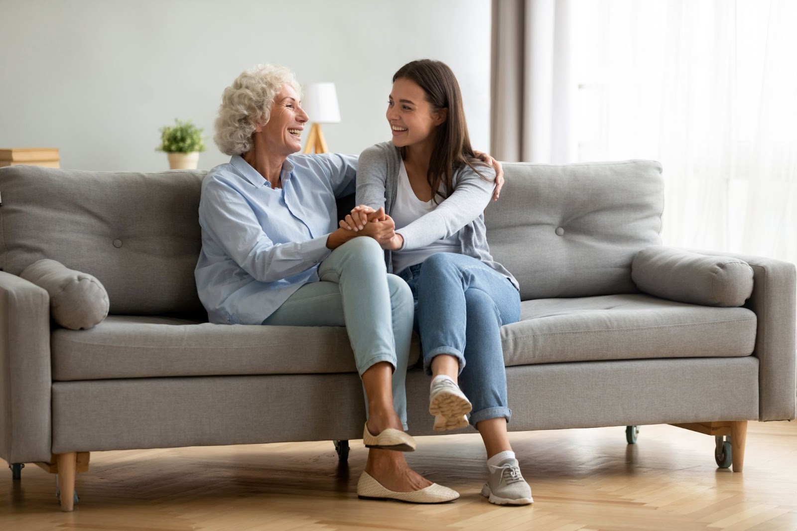Grandmother and granddaughter happily chatting on the couch at a senior living community.
