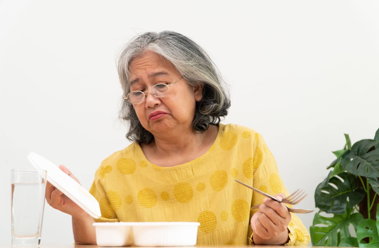 Senior woman looking disappointed with her meal, reflecting loss of appetite.