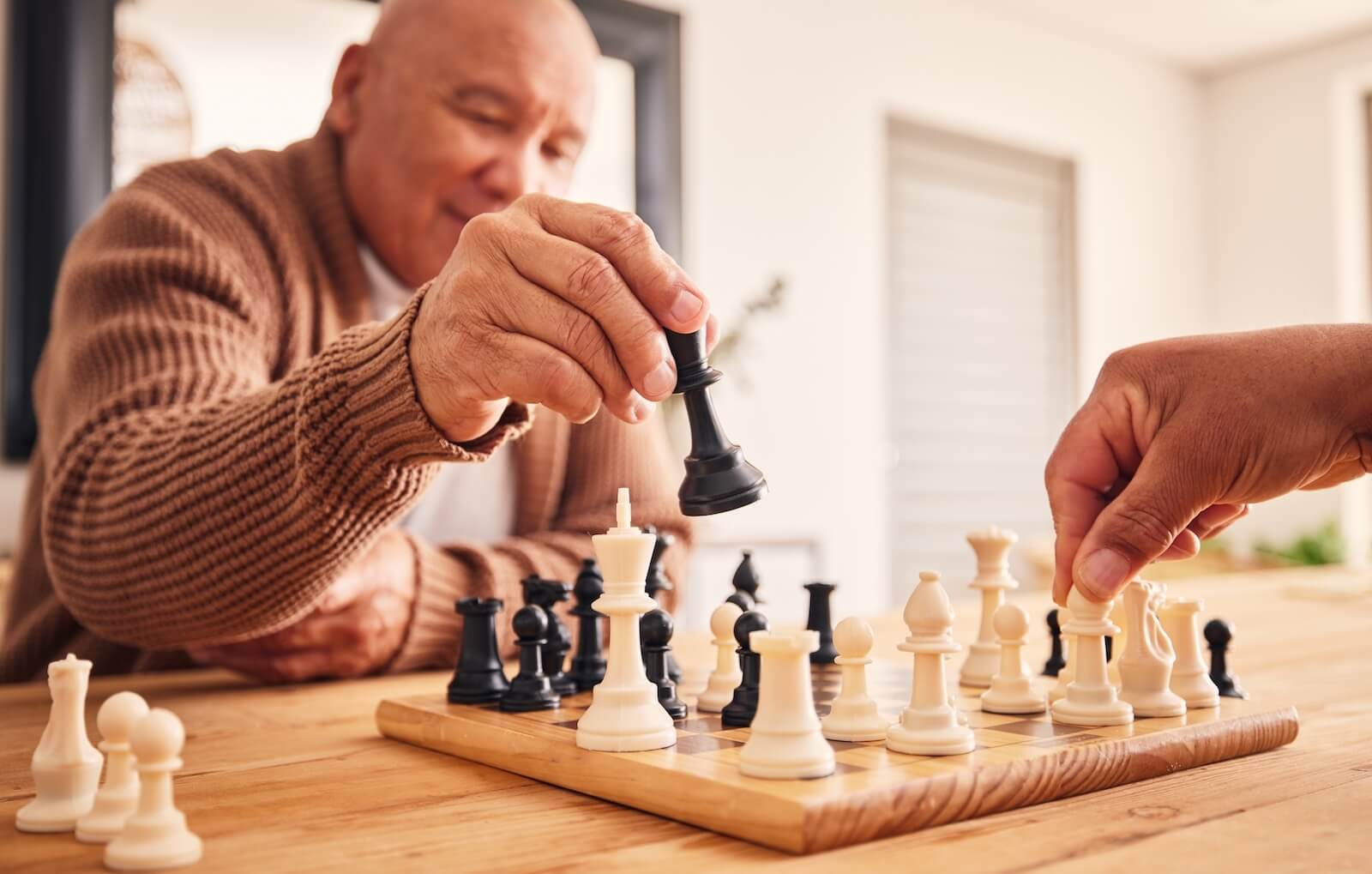 An older adult playing chess against an out-of-frame opponent in senior living to strengthen their brain.