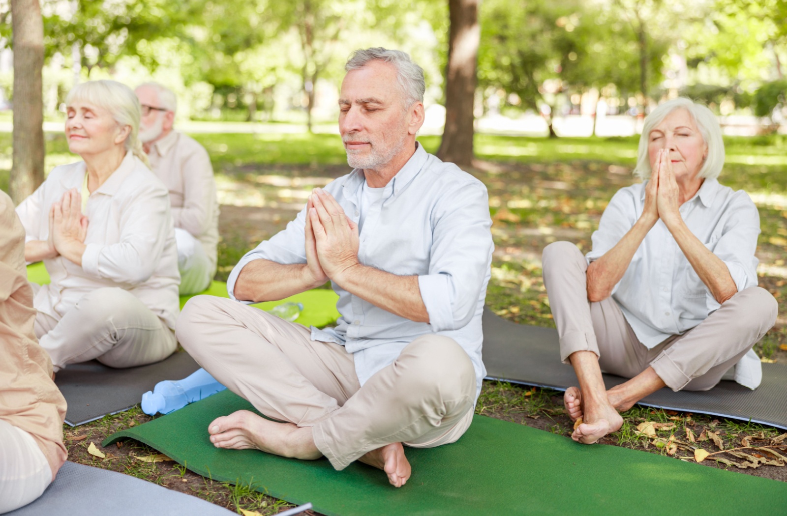 Seniors practicing breathing exercises outdoors on mats to improve lung health and well-being in a peaceful green setting.