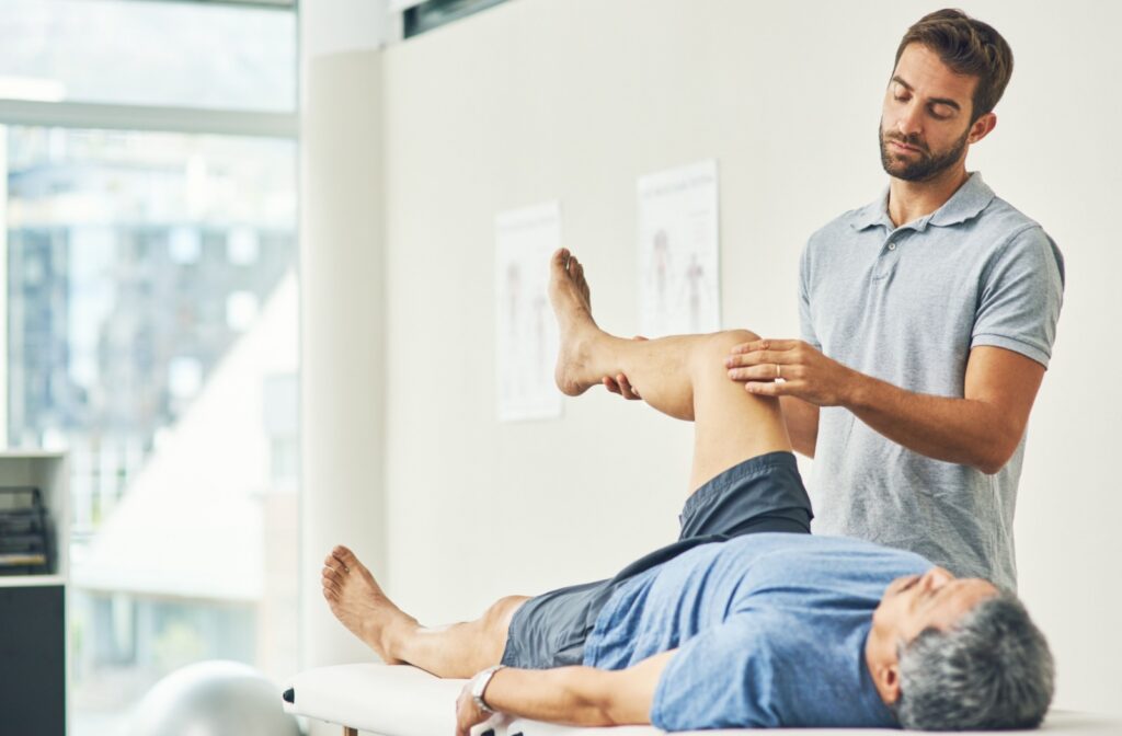 A physiotherapist shows a senior how to perform knee bends that they can perform in their bed at home.