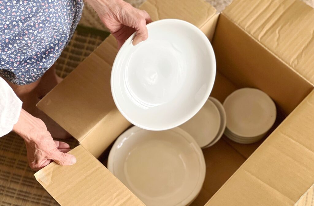 An older couple packing away white dishes into a moving box to prepare for senior living.