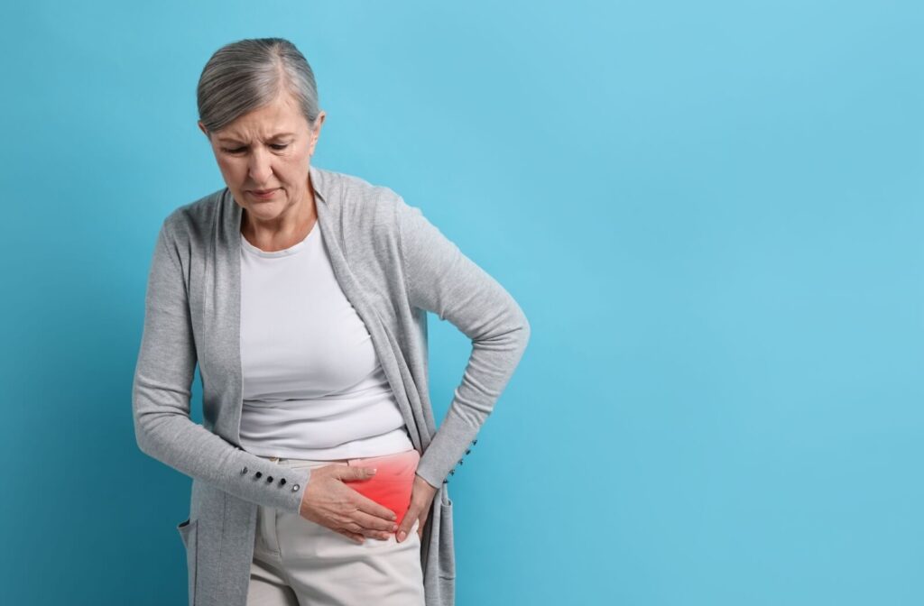 Against a blue background, a senior grimaces while holding their hip, highlighted in red to showcase hip pain