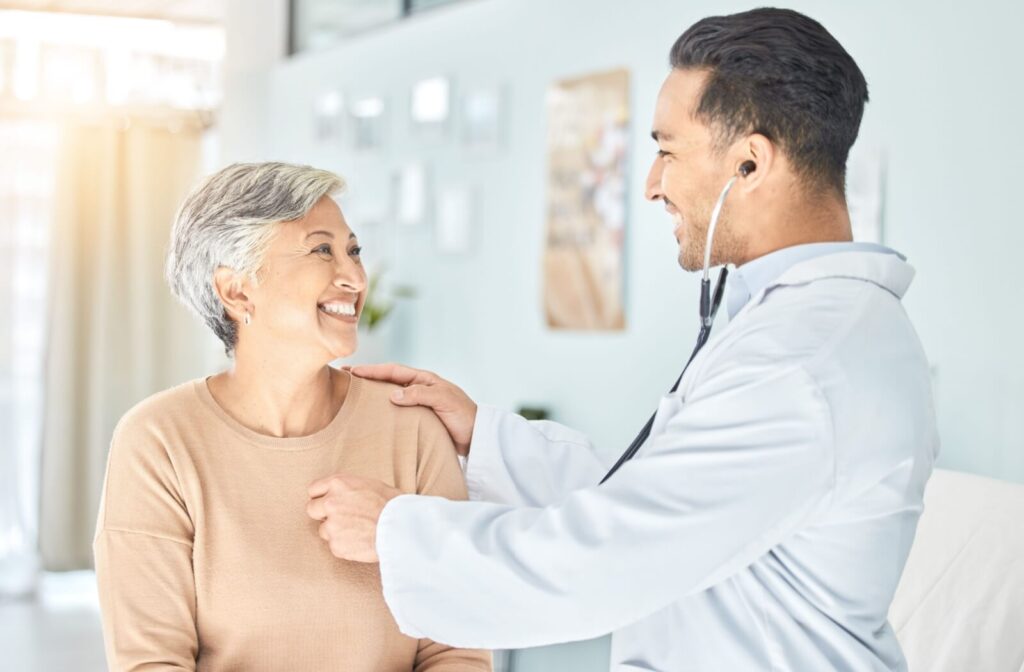 A senior smiles at their doctor as they listen to their heart during a routine check-up after a heart attack