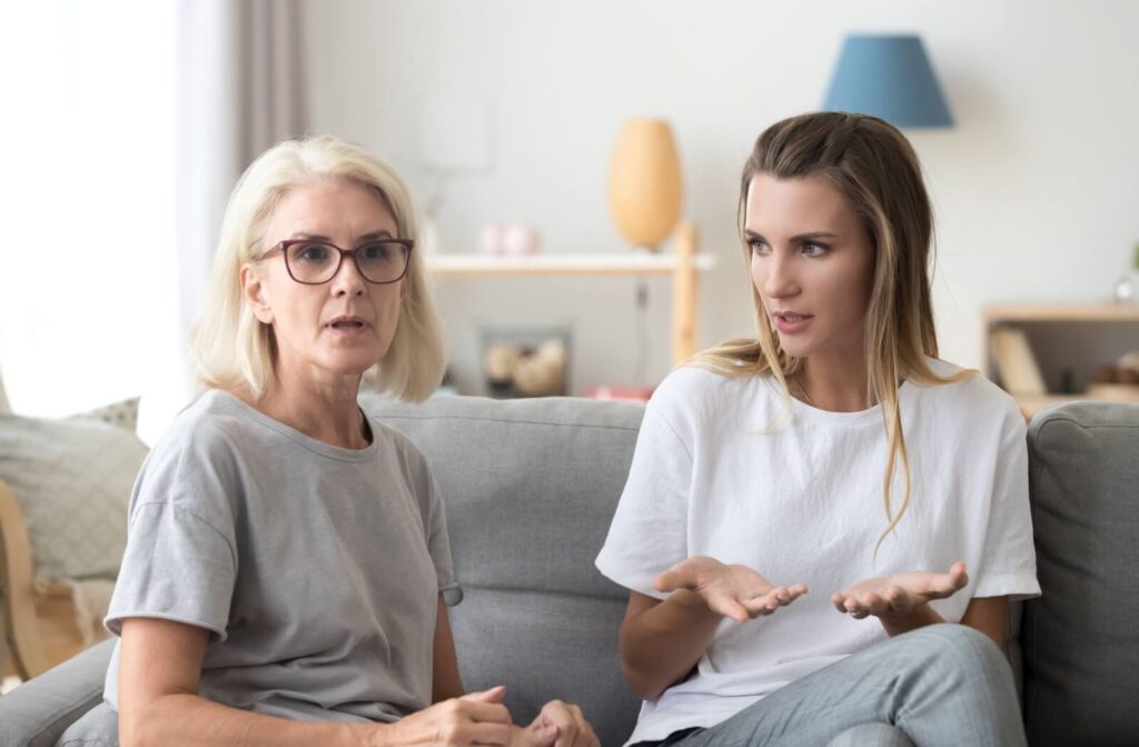 A senior and adult child sit on a couch in disagreement while discussing assisted living options
